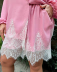 Pink garment with lace detailing worn by a person, with a blurred natural background.
