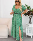 Woman wearing a green floral dress with a belt, standing in a room with a white couch and plant.